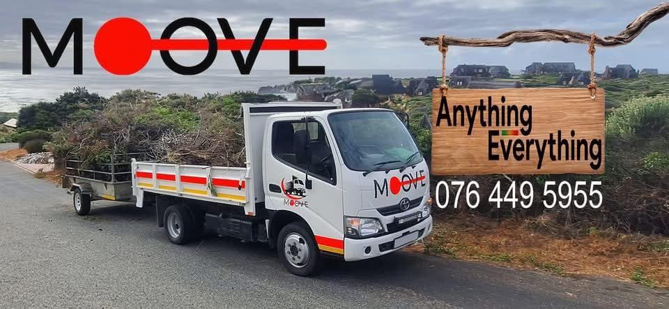 White Moove truck hauling garden waste on a coastal road with a wooden contact sign.