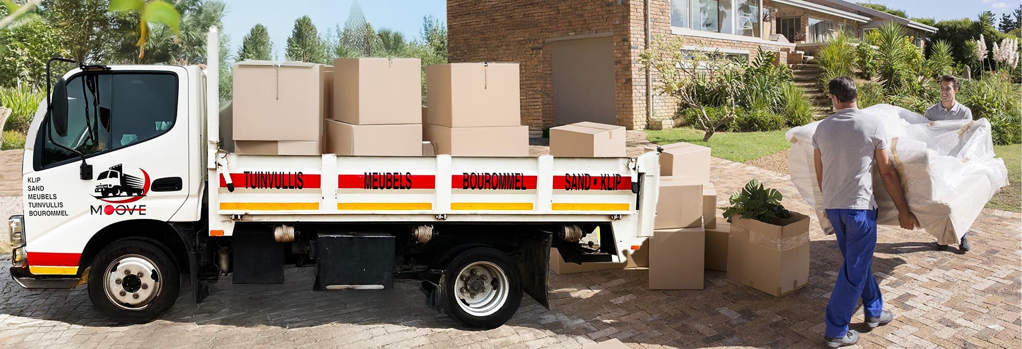 Movers carry wrapped furniture toward a white truck loaded with boxes in a residential driveway.