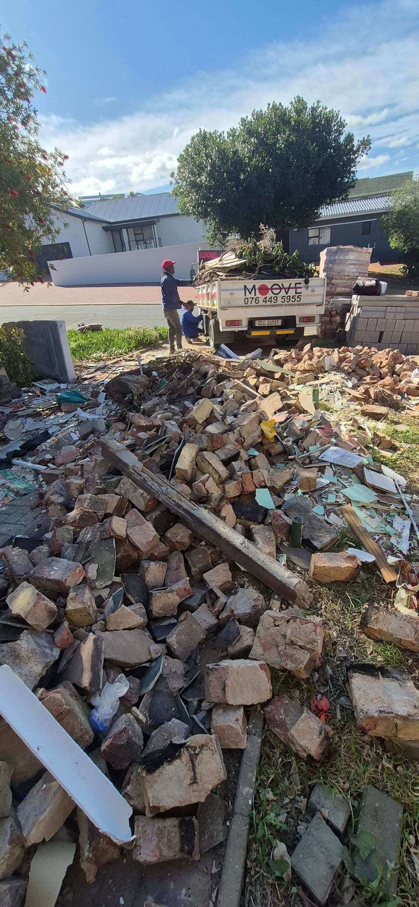 Workers load a waste truck behind a large pile of bricks and construction debris.
